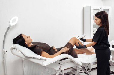 Kozmetik uzmanı kozmetoloji kabinesindeki kadın bacağının kıllarını aldırıyor..