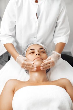 Kozmetolog kozmetoloji salonunda kadın yüzüne krem sürüyor..