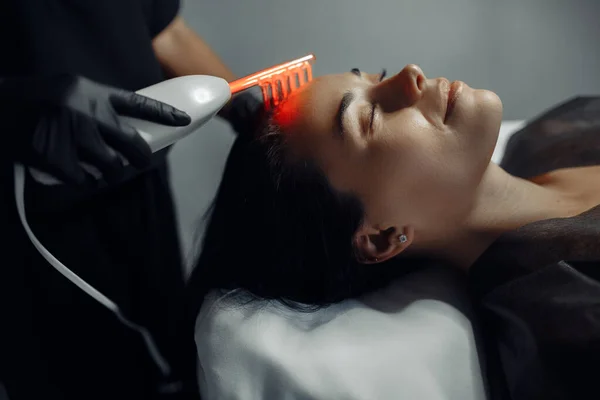 Cosmetólogo hace el procedimiento de terapia microcurrent en el cabello de una hermosa mujer joven en el salón de cosmetología . —  Fotos de Stock