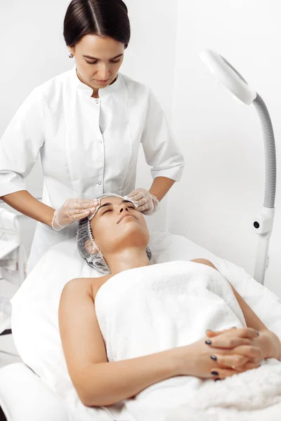 Cosmetólogo limpia la cara femenina antes de aplicar la crema en el salón de cosmetología . —  Fotos de Stock
