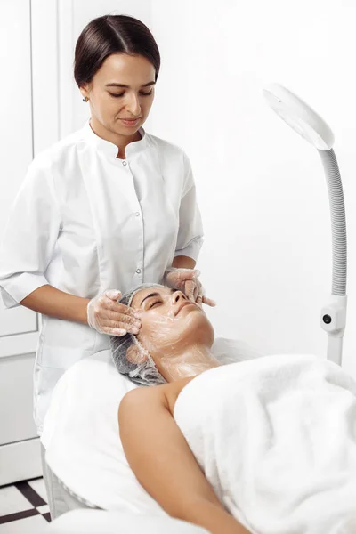 Cosmetólogo aplicar crema en la cara femenina en el salón de cosmetología . —  Fotos de Stock