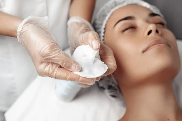 Cosmetologist aplicando creme no rosto feminino no salão de cosmetologia . — Fotografia de Stock