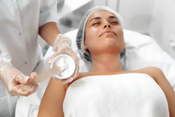 Cosmetoloog aanbrengen crème op vrouwelijk gezicht in cosmetologie salon. — Stockfoto