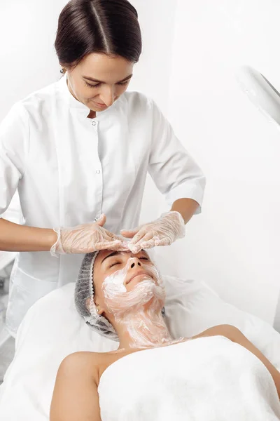 Kosmetolog stosujący krem na twarz kobiety w salonie kosmetologii. — Zdjęcie stockowe