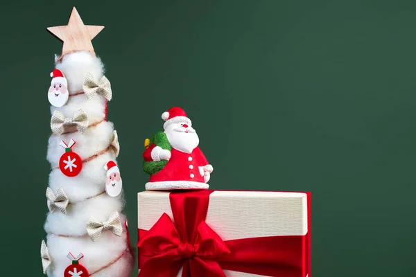 Gips bunte Weihnachtsmann auf der Geschenkbox und Weihnachtsbaum mit Dekorationen über grünem Hintergrund. — Stockfoto