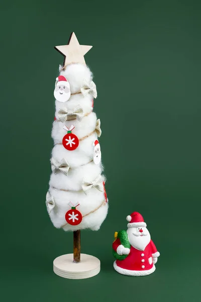 Gips bunte Weihnachtsmann und Weihnachtsbaum mit Dekorationen über grünem Hintergrund. Neujahrs- und Weihnachtskonzept. — Stockfoto