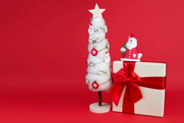 Schöne Dekoration aus Gips bunte Weihnachtsmann auf der Geschenkbox und Weihnachtsbaum auf rotem Hintergrund. — Stockfoto