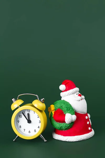 Niedlichen Gips bunten Weihnachtsmann und gelbe Uhr isoliert über grünem Hintergrund. Neujahrs- und Weihnachtskonzept. — Stockfoto