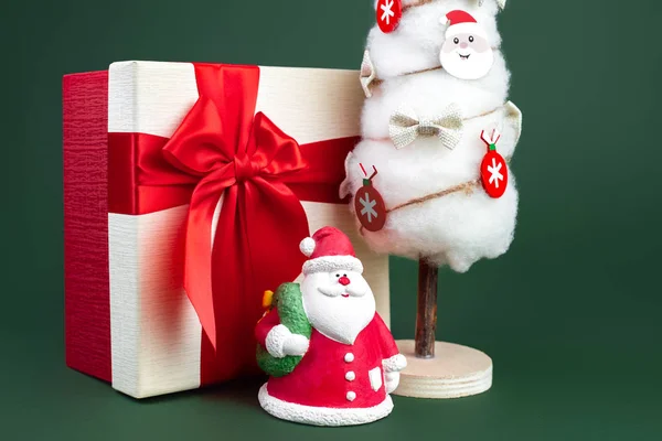 Nahaufnahme Foto von Gips bunten Weihnachtsmann auf der Geschenkbox und Weihnachtsbaum mit Dekorationen über grünem Hintergrund. — Stockfoto