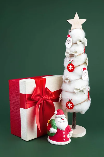 Gips bunte Weihnachtsmann auf der Geschenkbox und Weihnachtsbaum mit Dekorationen über grünem Hintergrund. Kopierraum — Stockfoto