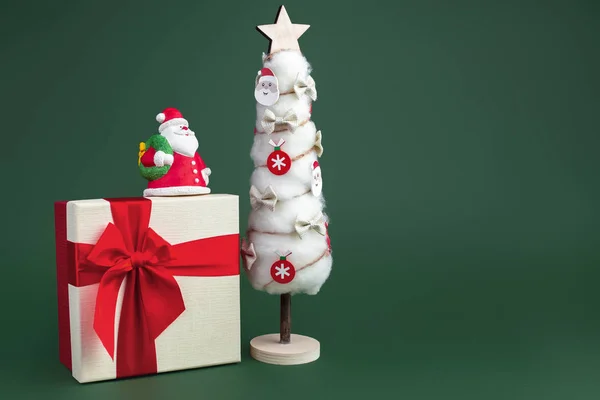 Gips bunte Weihnachtsmann auf der Geschenkbox und Weihnachtsbaum mit Dekorationen über grünem Hintergrund. Kopierraum — Stockfoto