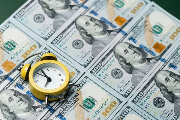 Yellow alarm clock on the stack of one hundred american dollars bills. Credit, deposit and mortgage concept.