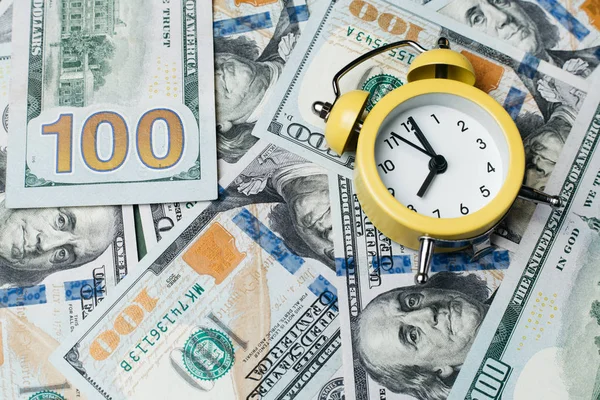 100ドル札のスタック上の黄色の目覚まし時計。信用、預金及び抵当の概念. — ストック写真