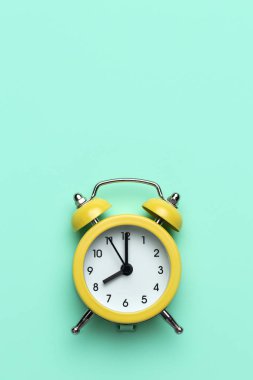 Cyan arka planda sarı yuvarlak alarm saati.