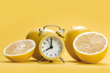 Limonlu meyve dilimi ve sarı arka planda limonlar. Limonların önündeki sarı alarmlı saat.