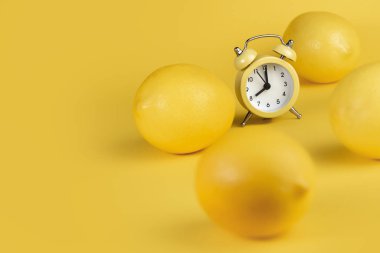 Limonlu meyve dilimi ve sarı arka planda limonlar. Limonların önündeki sarı alarmlı saat.
