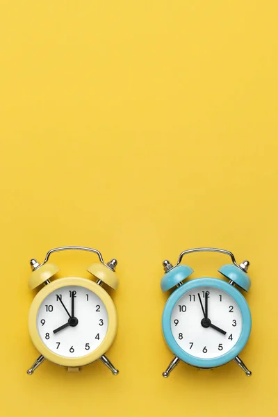 Dos relojes de alarma redondos amarillo y azul sobre el fondo amarillo . —  Fotos de Stock