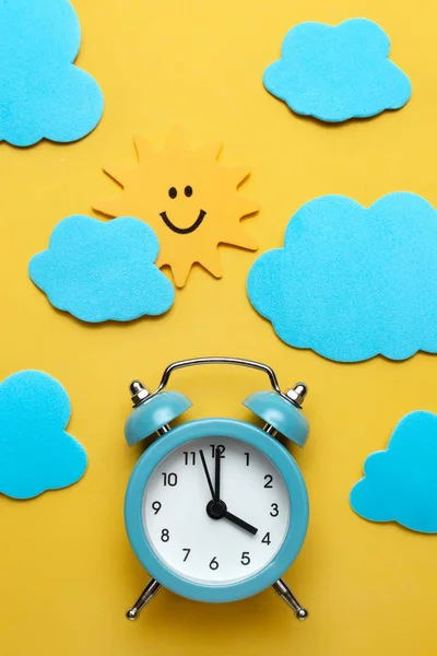 Blå rund väckarklocka, sol och moln på den gula bakgrunden. — Stockfoto