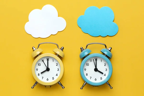 Dos relojes de alarma redondos amarillo y azul y nubes en el fondo amarillo . —  Fotos de Stock