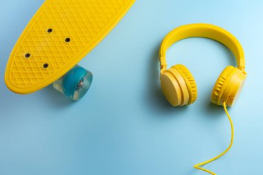Sarı kulaklıklar ve kaykay veya blue arka plan üzerinde pennyboard. Müzik konsepti.