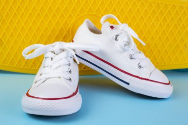 Mavi arka plan üzerinde kaykay veya penny board önünde beyaz spor ayakkabı.
