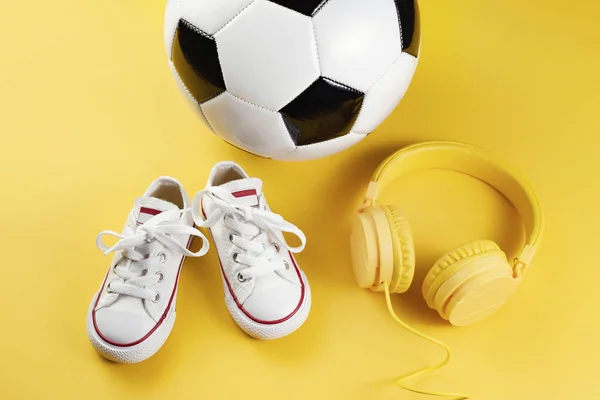 黄色耳机、白色运动鞋和传统足球风格在黄色背景下的特写照片. — 图库照片