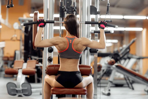 Jeune femme travaillant à la machine de traction lat dans la salle de gym. Sport, fitness, powerlifting et concept de personnes — Photo