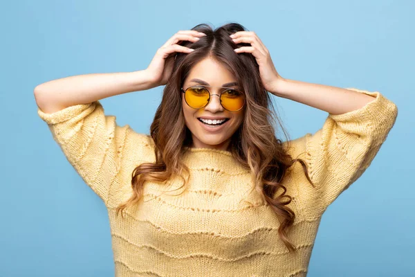 Vonzó fiatal nő pózol kék alapon sárga pulóver. Csinos lány a sárga szemüveg. — Stock Fotó