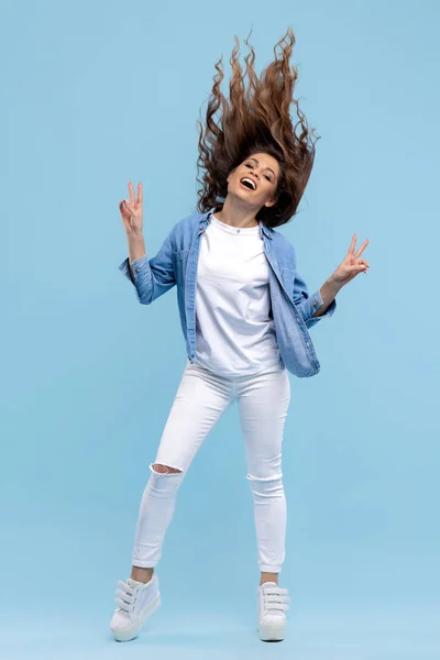 Encantadora joven con sonrisa brillante vestida con ropa moderna y elegante bailando con el pelo sobre fondo azul . — Foto de Stock