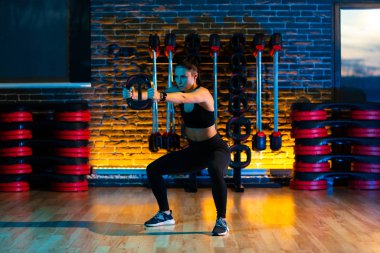 Sağlıklı genç kadın spor salonunda ağırlık plakalarıyla egzersiz yapıyor..