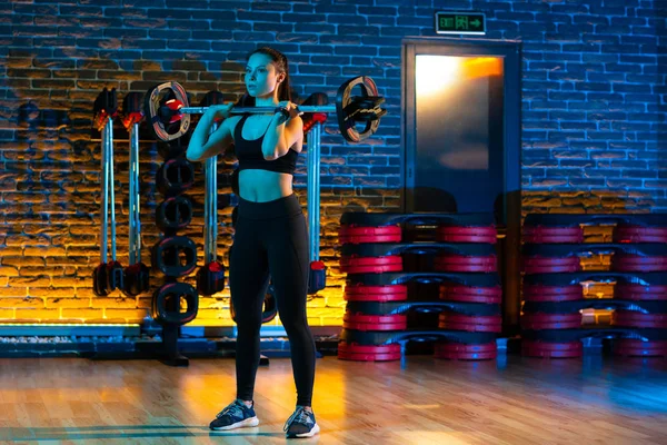 Ganzkörperaufnahme einer gesunden jungen Frau, die im Fitnessstudio Übungen mit der Langhantel macht. Gesundheits- und Sportkonzept. — Stockfoto