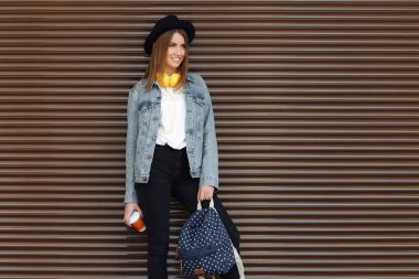 Kahverengi saçlı, şapkalı, sırt çantalı ve açık havada sarı tonlu sevimli bir kız. Müzik dinleyen genç bir kadın.