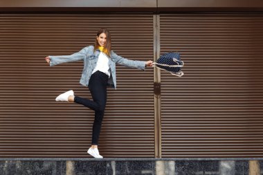 Kahverengi saçlı, sırt çantalı ve açık havada sarı kulaklıklı mutlu bir kız. Özgürlük kavramı.