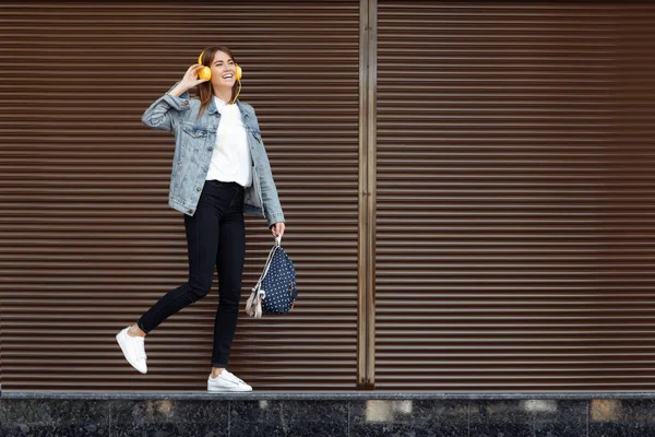 茶色い髪で陽気笑顔の女の子は、屋外でバックパックと黄色の電話を身に着けています。自由の概念. — ストック写真