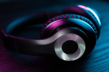 Koyu ahşap arka planda siyah kulaklık. Neon ışıkta kablosuz kulaklık..