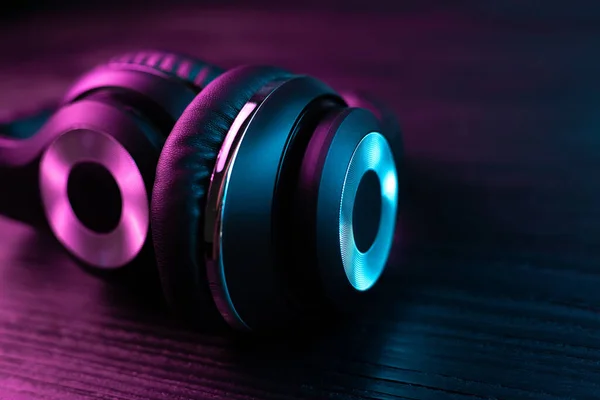 Black headphone on dark wooden background. Stylish wireless headset in neon light. — Stock Photo, Image