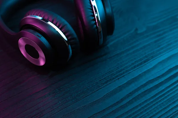 Auriculares negros sobre fondo de madera oscura. Auriculares inalámbricos con estilo en luz de neón . —  Fotos de Stock