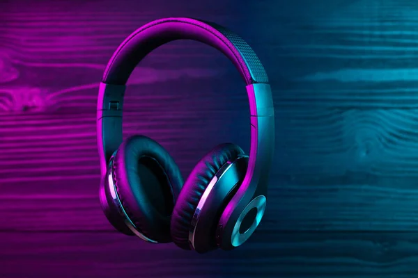 Black headphone on dark wooden background. Stylish wireless headset in neon light. — 스톡 사진
