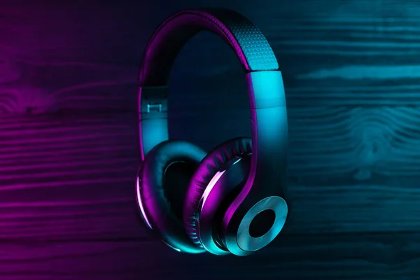 Black headphone on dark wooden background. Stylish wireless headset in neon light. — 스톡 사진