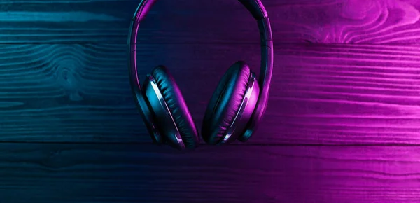 Fekete fejhallgató sötét fából készült háttérrel. Stílusos vezeték nélküli fejhallgató neon fényben. — Stock Fotó