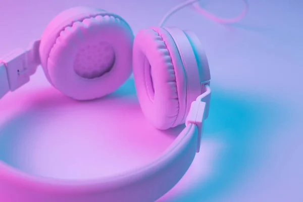 Foto in stile retrò anni '90 di eleganti cuffie wireless bianche in luci al neon. Concetto musicale . — Foto Stock