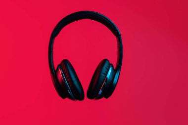 Retro 90s style photo of black stylish modern wireless headphone in neon lights over red background.