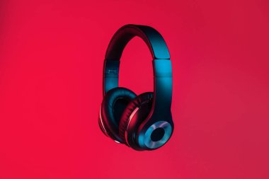 Retro 90s style photo of black stylish modern wireless headphone in neon lights over red background.