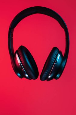 Retro 90s style photo of black stylish modern wireless headphone in neon lights over red background.