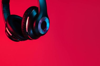 Close-up shot of retro 90s style photo of black stylish modern wireless headphone in neon lights over red background.