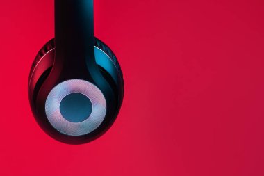 Close-up shot of retro 90s style photo of black stylish modern wireless headphone in neon lights over red background.