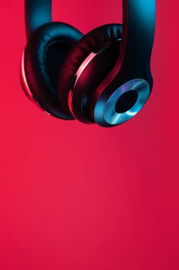 Retro 90s style photo of black stylish modern wireless headphone in neon lights over red background.