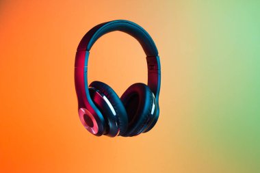 Retro 90s style photo of black stylish modern wireless headphone in neon lights over colorful background.