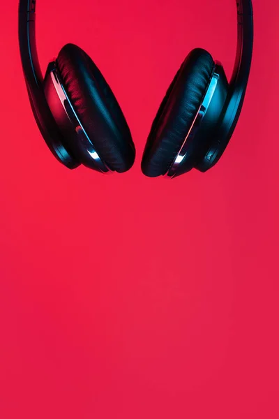 Retro 90s style photo of black stylish modern wireless headphone in neon lights over red background. — 图库照片