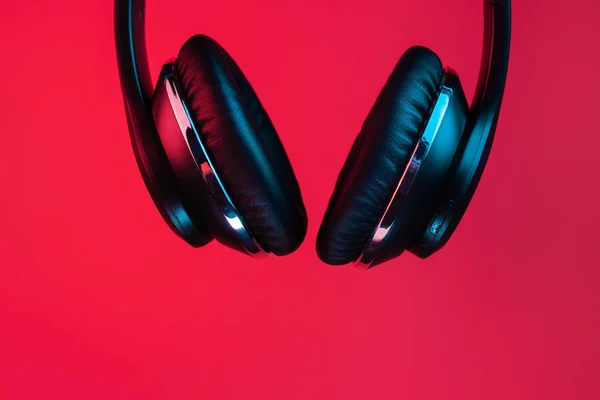 Retro 90s style photo of black stylish modern wireless headphone in neon lights over red background. — Stockfoto